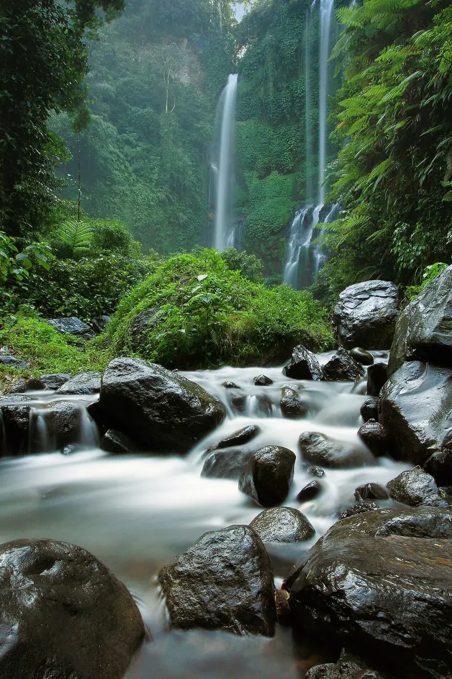 The tall Sekumpul waterfalls behind rocks in the river